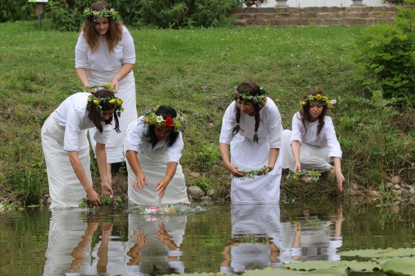 Pięć kobiet w białych sukniach puszcza wianki na wodę