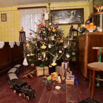 Wnętrze świąteczne w chałupie wiejskiej - choinka, pod nią zabawki: drewniana ciuchcia, klocki; na komodzie pomarańcze