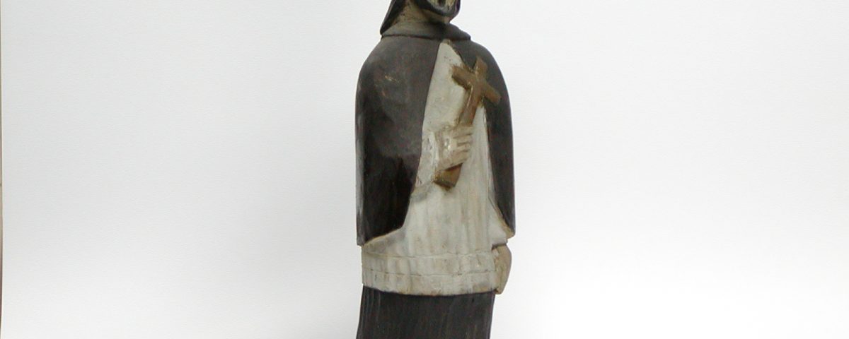drewniana rzeźba św. Jana Nepomucena w czarno-białym odzieniu trzymającego w dłoni krzyż