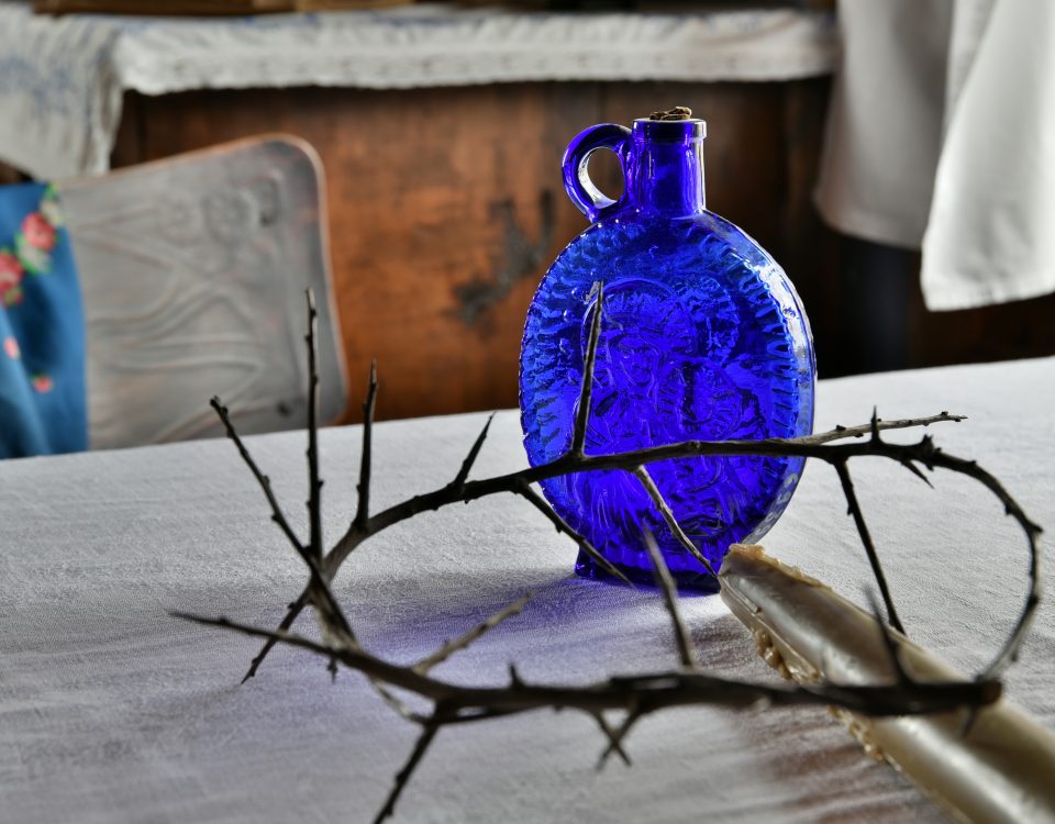 woda święcona w niebieskiej karafce i korona cierniowa na stole pod białym obrusem